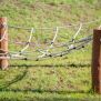 Diamond net playground climbing structure made of ropes and wooden posts on grass.